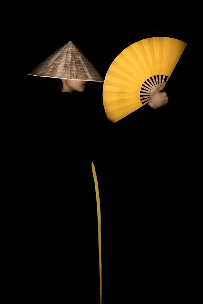 A lady with yellow fan wearing black and yellow ao dai in Vietnam