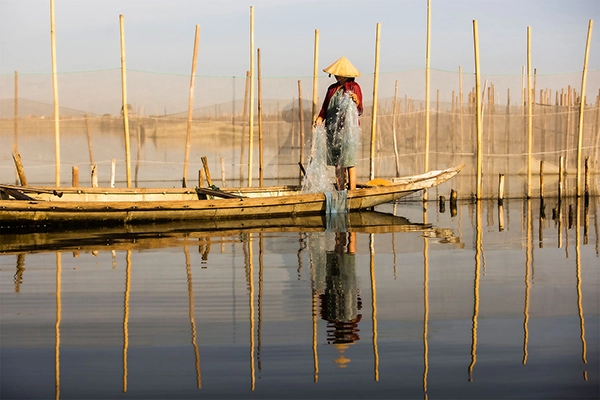 Vietnamese fisherman standing on a boat in a lagoon with fishing nets and bamboo poles