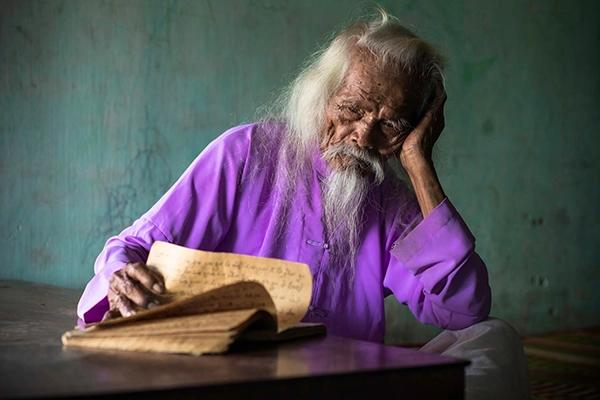 Elderly Vietnamese man reading an old book at a wooden table
